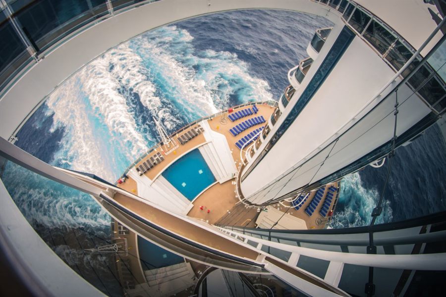 Looking down from a high deck at a cruise ship pool and the white wake of the sea