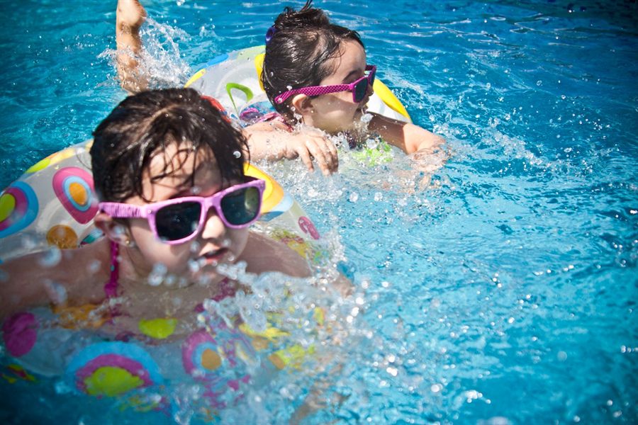 Two young girls in sunglasses splashing in a bright blue pool with a float