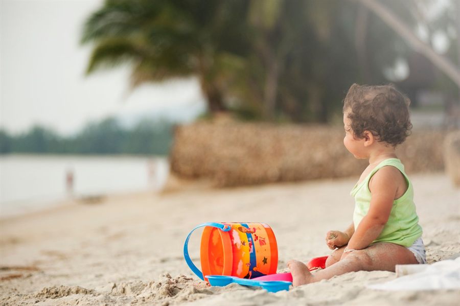 Toddler playing with a bucket and spade on a tropical beach