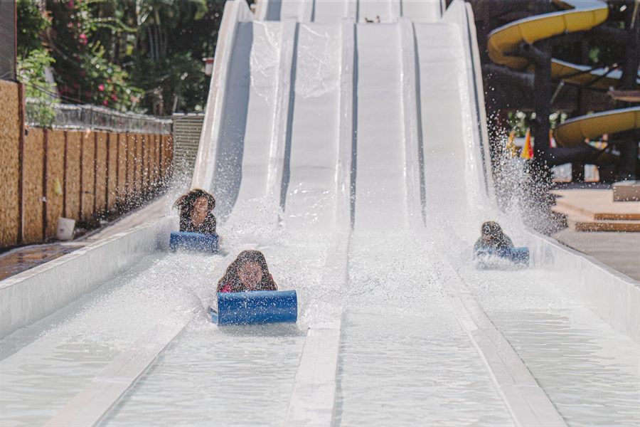 Children racing down a wide white water slide on mats