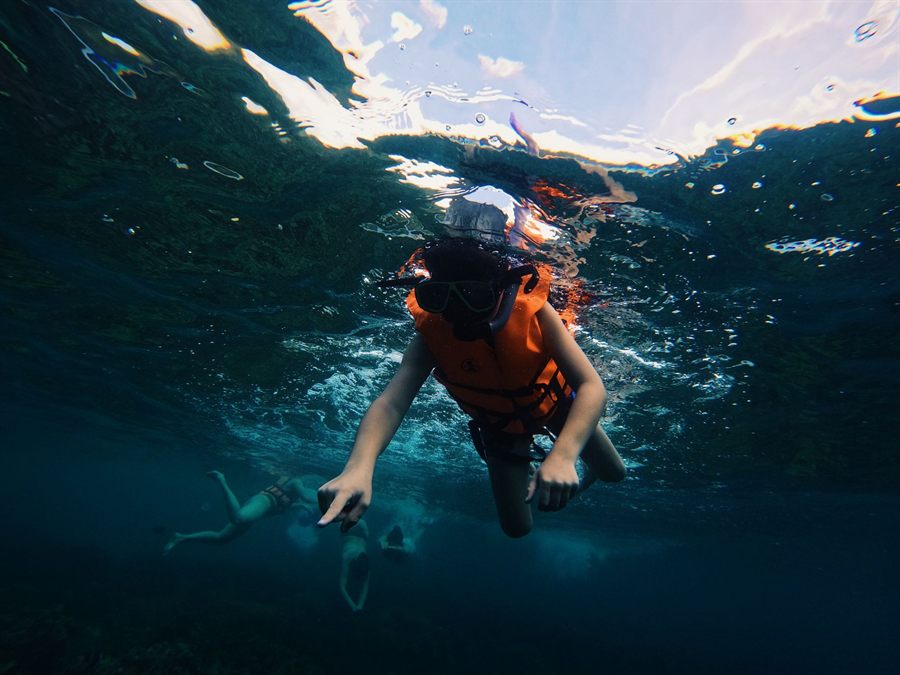 Child in an orange life vest snorkeling in clear blue water