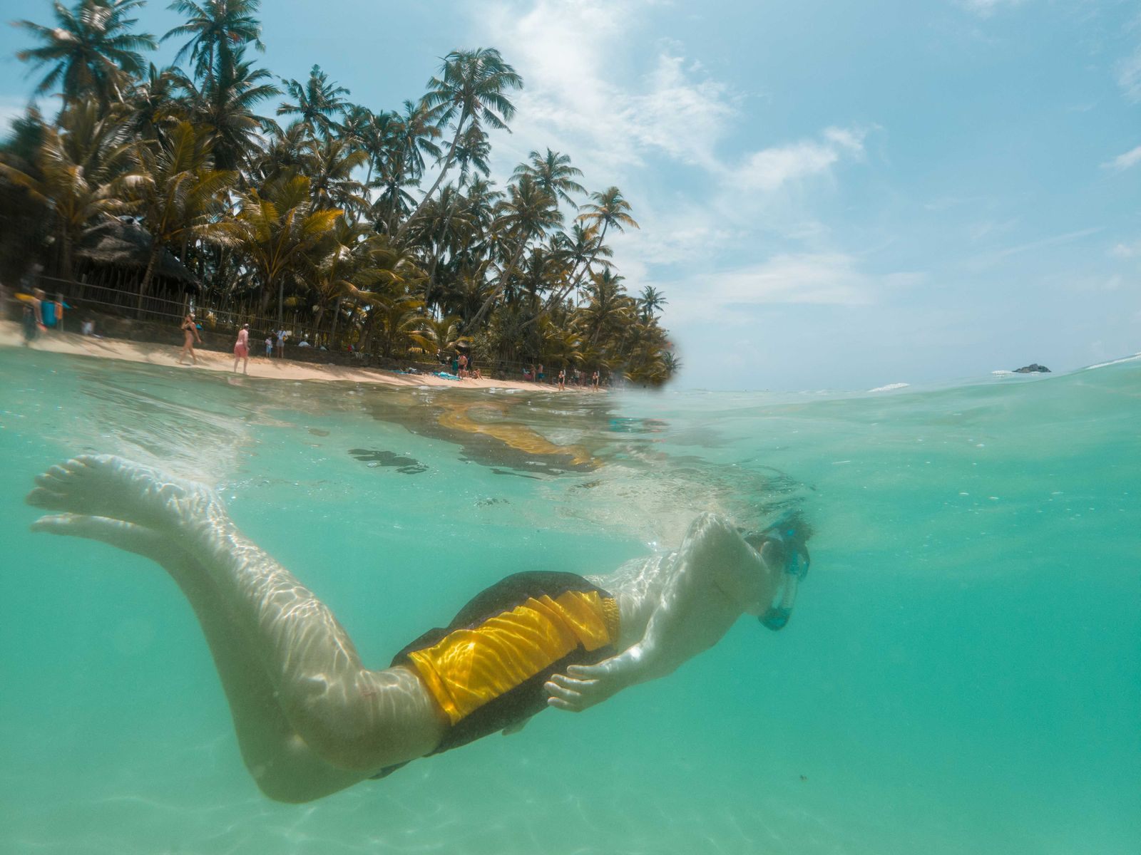 Teenager snorkeling in clear water off a palm-lined tropical beach