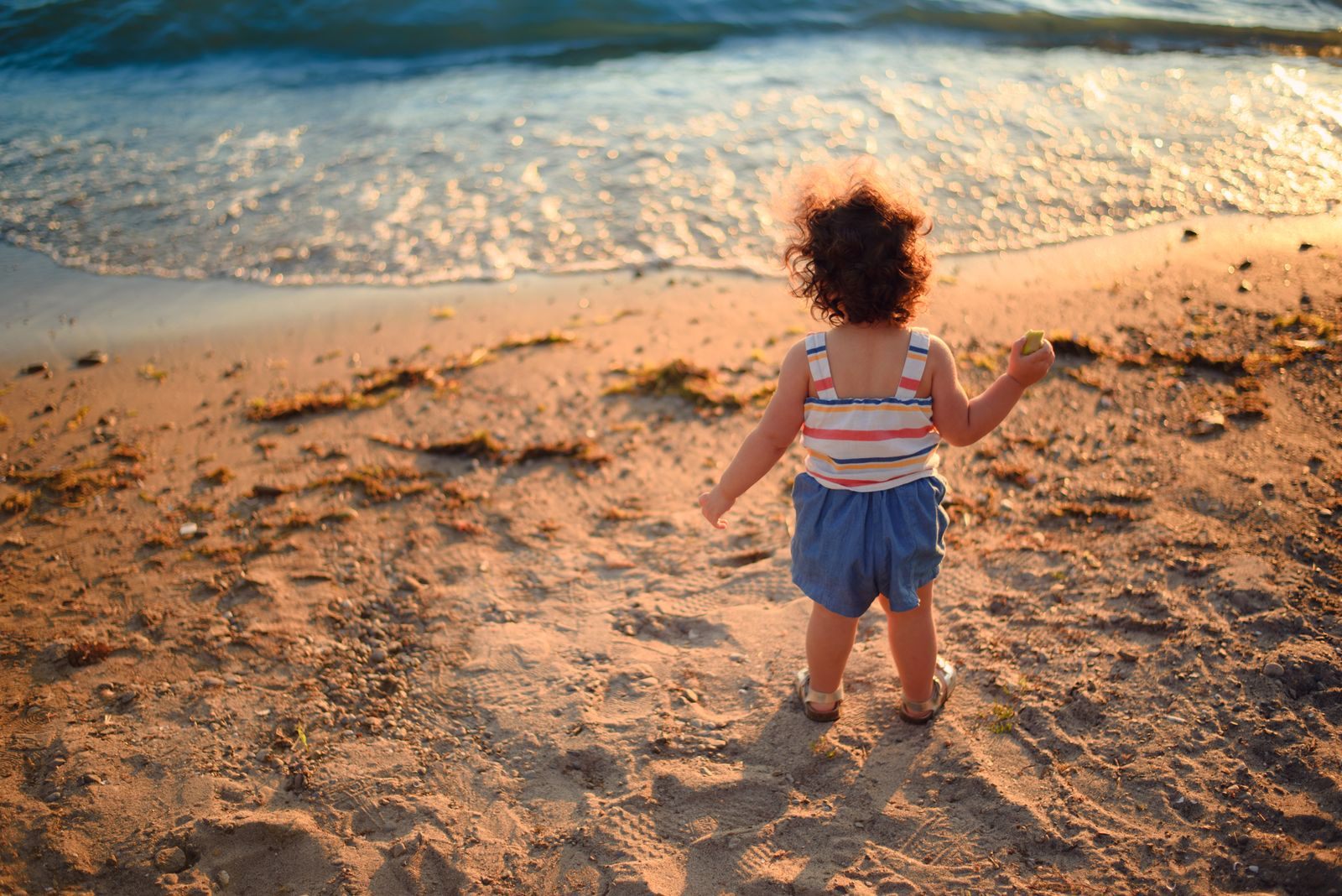 Toddler walking on a sandy beach toward the waves at sunset